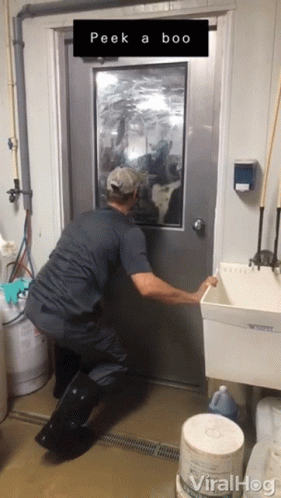 A Man Opens A Door With A Sign That Says Peek A Boo On It GIF