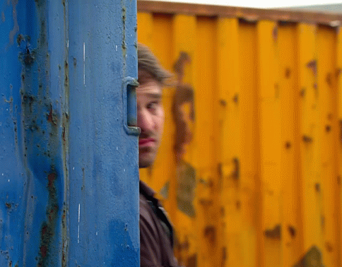 a man peeking out from behind a blue and yellow wall