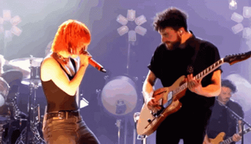 A Man Playing A Guitar And A Woman Singing Into A Microphone GIF