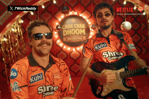 a man playing a guitar and another man playing drums in front of a sign that says chak chak dhoom