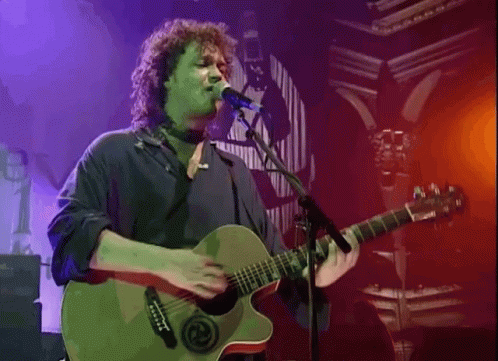 A Man Playing A Guitar And Singing Into A Microphone GIF