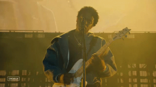 A Man Playing A Guitar And Singing Into A Microphone With A Sign That Says Canchella On The Bottom Right GIF