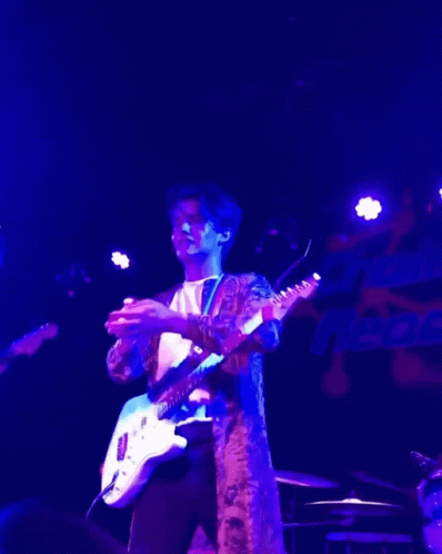 A Man Playing A Guitar In A Dark Room With Purple Lights GIF