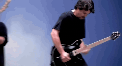 A Man Playing A Guitar In Front Of A Blue Wall GIF