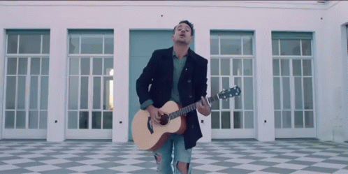 A Man Playing A Guitar In Front Of A Building GIF
