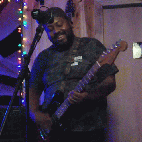 A Man Playing A Guitar In Front Of A Microphone With A Sign On The Wall That Says No Smoking GIF