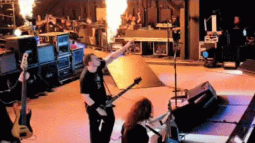 A Man Playing A Guitar On A Stage With Flames Coming Out Of It . GIF