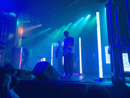 A Man Playing A Guitar On Stage With A Crowd Watching GIF