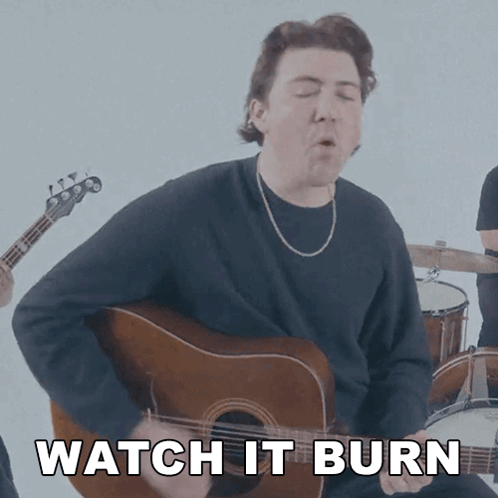 A Man Playing A Guitar With The Words " Watch It Burn " Behind Him GIF