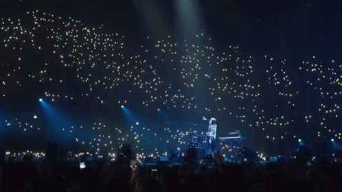 A Man Playing A Keyboard On A Stage With A Crowd Behind Him GIF