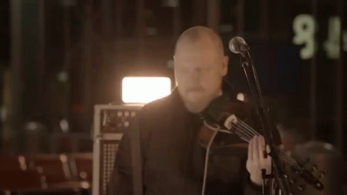 A Man Playing A Violin In Front Of A Microphone With The Number 9 On The Wall Behind Him GIF