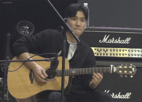 A Man Playing An Acoustic Guitar In Front Of A Marshall Amp GIF