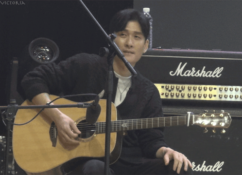 A Man Playing An Acoustic Guitar In Front Of A Marshall Amp GIF