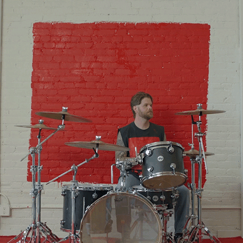A Man Playing Drums In Front Of A Red Wall GIF