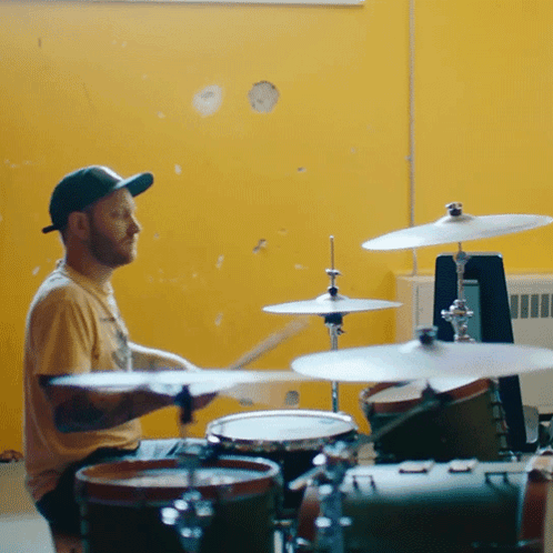 A Man Playing Drums With A Yellow Wall Behind Him GIF