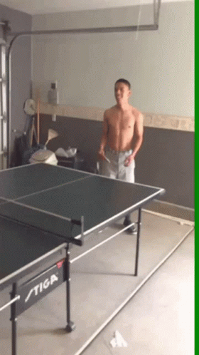 a man playing ping pong on a stiga table in a garage
