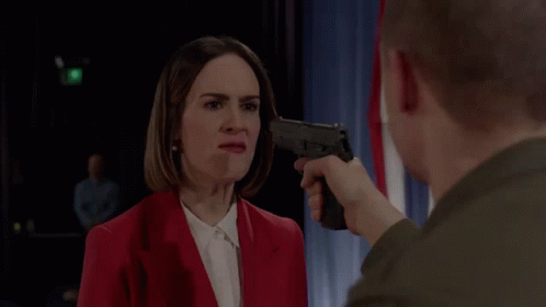 A Man Pointing A Gun At A Woman In A Red Jacket GIF