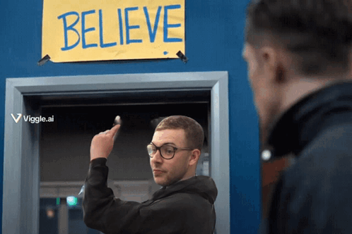 A Man Points To A Sign That Says Believe On It GIF