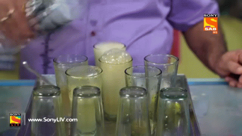 A Man Pouring A Drink Into A Tray Of Empty Glasses With A Sony Logo On The Bottom GIF