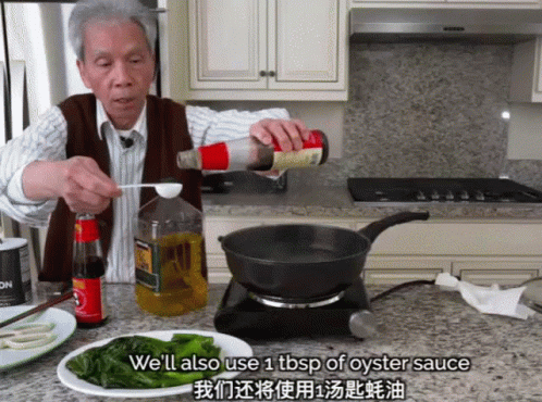 A Man Pouring Oyster Sauce Into A Frying Pan In A Kitchen GIF