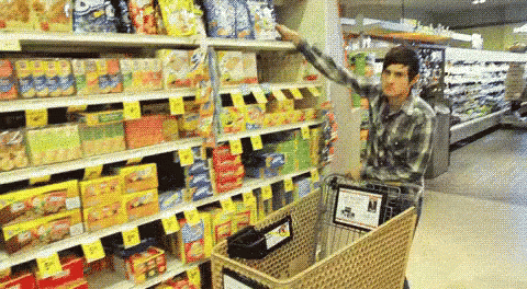 A Man Pushes A Shopping Cart Through A Grocery Store Aisle GIF