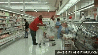 A Man Pushing A Shopping Cart Through A Grocery Store Aisle . GIF