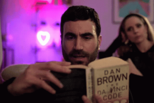 A Man Reading A Book By Dan Brown GIF