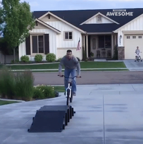 A Man Rides A Bike Down A Ramp In Front Of A House That Says Awesome GIF