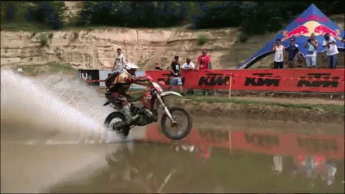 A Man Riding A Dirt Bike In The Water With A Ktm Sign In The Background GIF