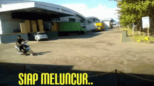 A Man Riding A Motorcycle In Front Of A Warehouse With The Words Siap Meluncur Written On The Bottom GIF