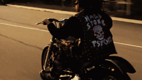 A Man Riding A Motorcycle With A Jacket That Says Psycho On It GIF
