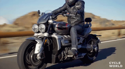 A Man Riding A Triumph Motorcycle On The Road GIF