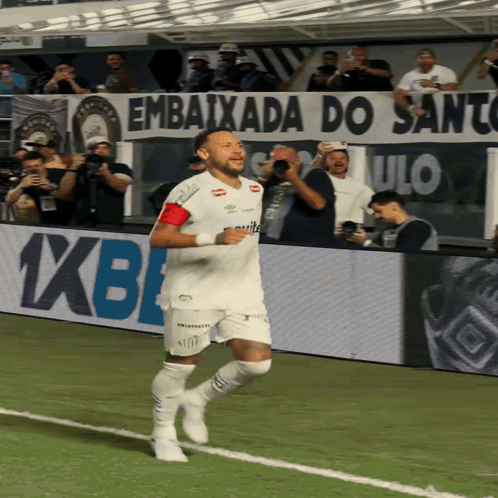 a man running on a soccer field with a banner behind him that says " embaixada do santos "