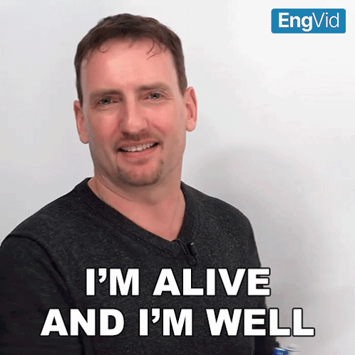 A Man Says " I 'M Alive And I 'M Well " In Front Of A White Wall GIF