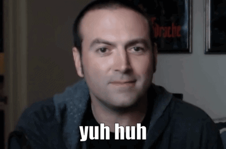 A Man Says Yuh Huh In Front Of A Wall With Pictures On It GIF