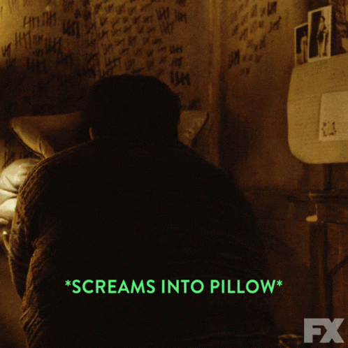A Man Screams Into A Pillow In A Dark Room GIF