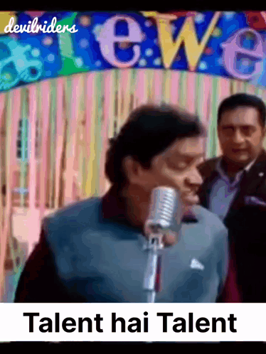 A Man Singing Into A Microphone In Front Of A Banner That Says Talent Hai Talent GIF