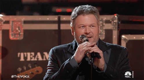 A Man Singing Into A Microphone In Front Of A Box That Says Team GIF