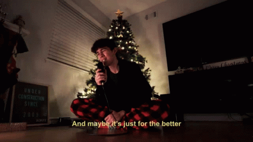 A Man Singing Into A Microphone In Front Of A Christmas Tree With The Words And Maybe It 'S Just For The Better GIF
