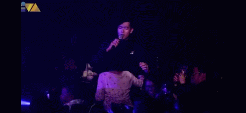 a man singing into a microphone in front of a crowd in a dark room