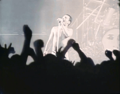 A Man Singing Into A Microphone In Front Of A Crowd Of People GIF