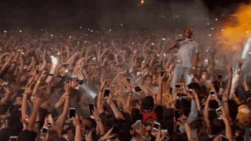 A Man Singing Into A Microphone In Front Of A Crowd Of People Holding Up Their Phones GIF