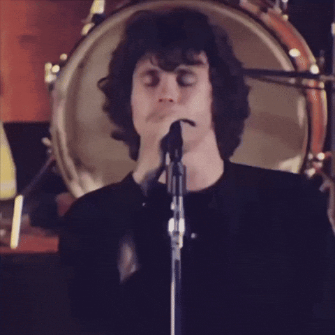 A Man Singing Into A Microphone In Front Of A Drum Set GIF
