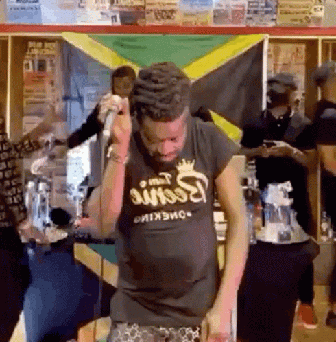 A Man Singing Into A Microphone In Front Of A Jamaican Flag GIF