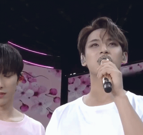 A Man Singing Into A Microphone In Front Of A Pink Background GIF
