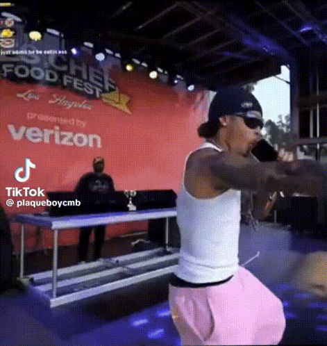 A Man Singing Into A Microphone In Front Of A Sign That Says Food Fest GIF
