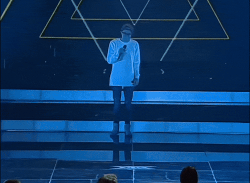 A Man Singing Into A Microphone Wearing A Hat And Glasses GIF