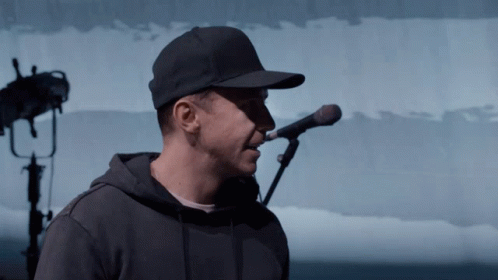A Man Singing Into A Microphone Wearing A Hat GIF