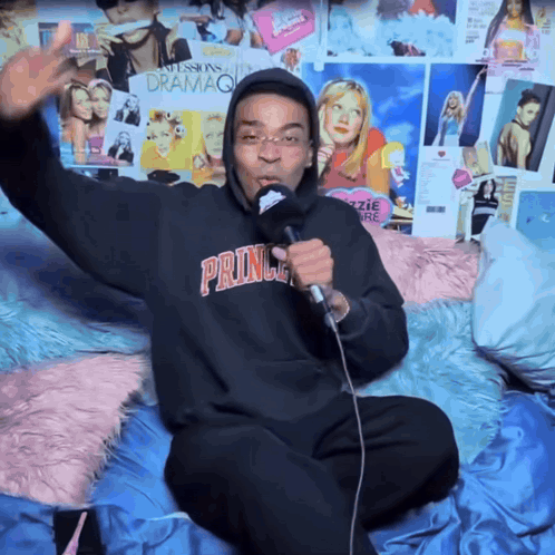 A Man Singing Into A Microphone Wearing A Prince Hoodie GIF