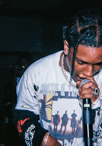 A Man Singing Into A Microphone Wearing A Shirt That Says ' Aootie & Tan ' GIF